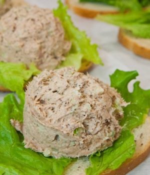 This is a close up shot of a scoop of fresh tuna salad resting on top of a lettuce leaf. The lettuce and tuna are also resting on a piece of bread.